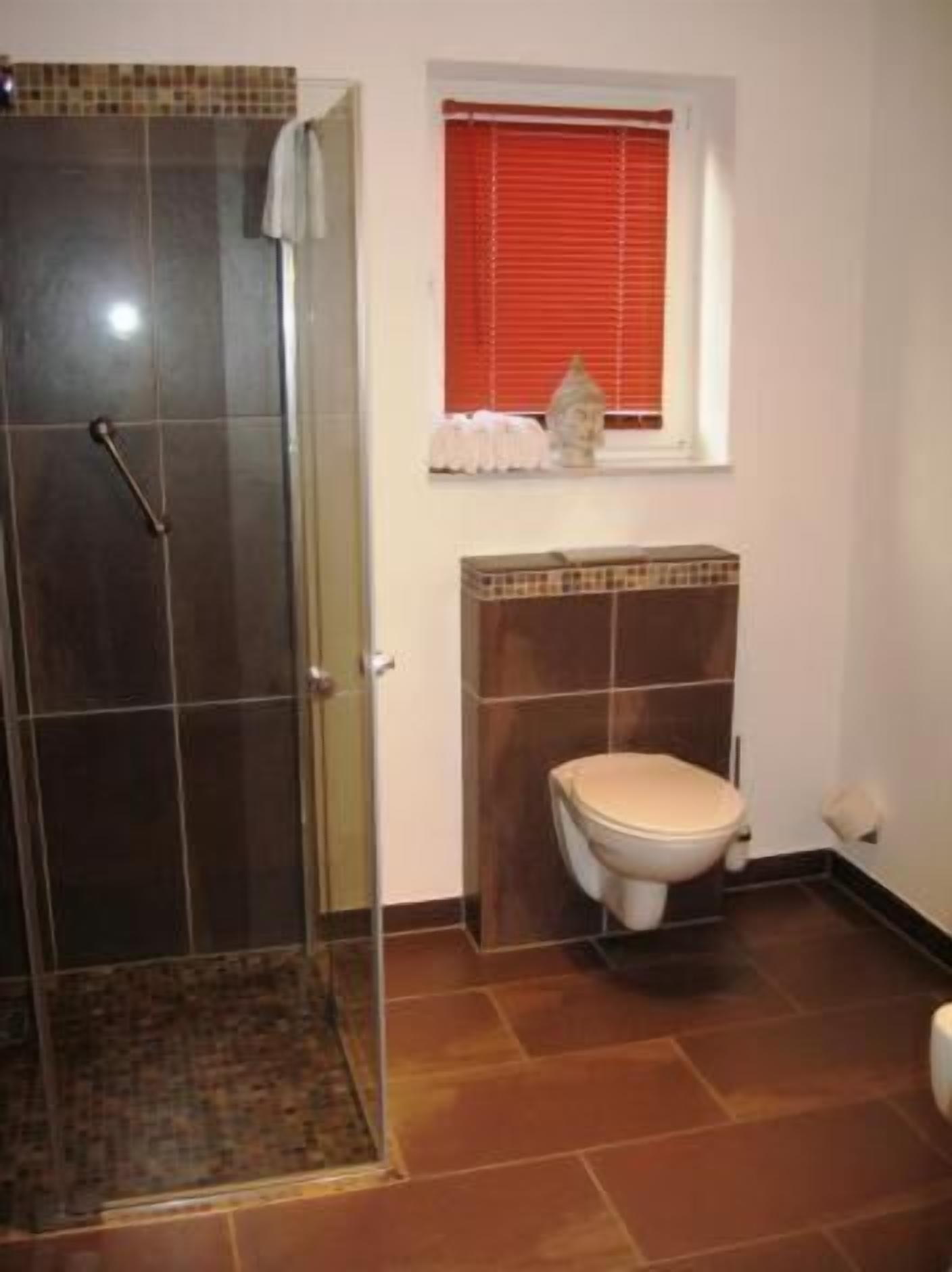Ein Badezimmer mit Dusche, Toilette und einem Fenster mit Jalousien.
