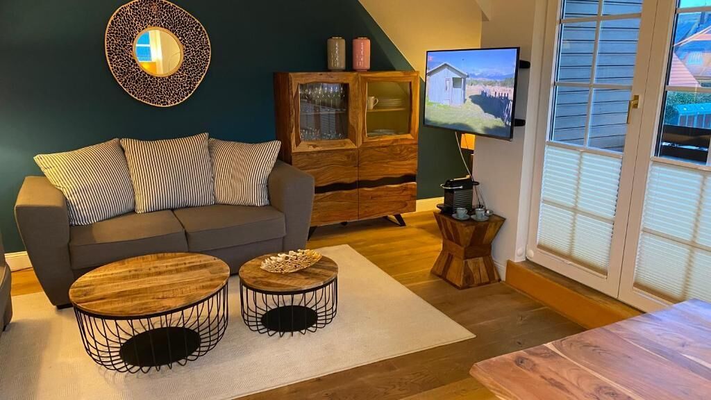 A living room with a sofa, two round coffee tables, a wooden cabinet, a television, and a window with blinds.