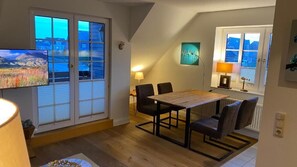 Un comedor con mesa y sillas de madera, un televisor a la izquierda y vistas a la montaña a través de las ventanas.