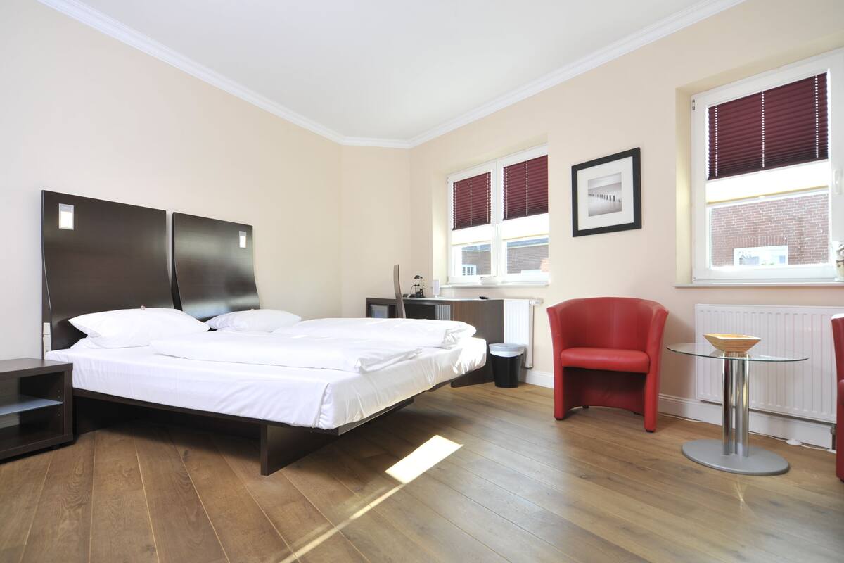 A modern bedroom with a bed, a red chair, a small table, and a window with blinds.