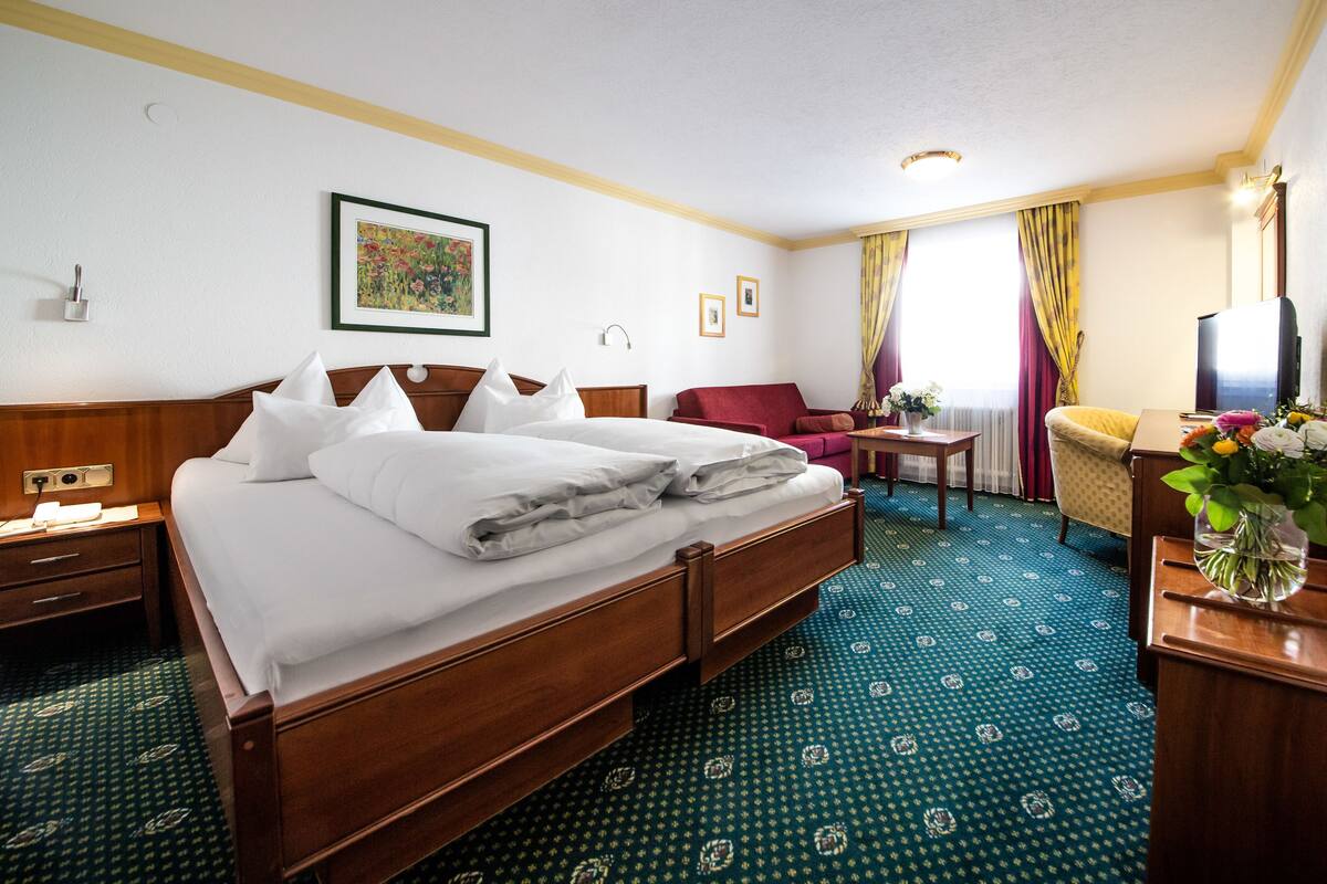 Une chambre d’hôtel avec un grand lit, un bureau, une chaise, une télévision et un vase rempli de fleurs.