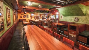 A restaurant with wooden tables and booths, a bar area, and a green textured wall. - Hotel Kristall (Sankt Anton am Arlberg)
