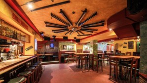 A bar with multiple stools and tables, a brick wall with a neon sign, and a ceiling with exposed beams. - Hotel Kristall (Sankt Anton am Arlberg)