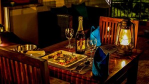 A dining table set with a bottle of champagne, two wine glasses, a plate of appetizers, a lantern, and a blue napkin. - Airavata Boutique Resort (Kandy)