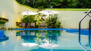 A swimming pool with two umbrellas, lounge chairs, and a reflection of the surrounding greenery. - Airavata Boutique Resort (Kandy)