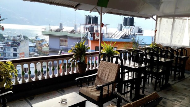 Una terraza con mesas al aire libre, macetas con plantas y vistas a edificios y depósitos de agua al fondo.