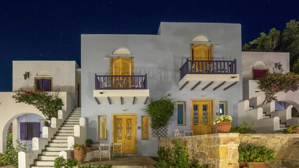 A two-story building with a balcony, a staircase, and a stone wall with plants. - Hotel Nefeli (Leros)