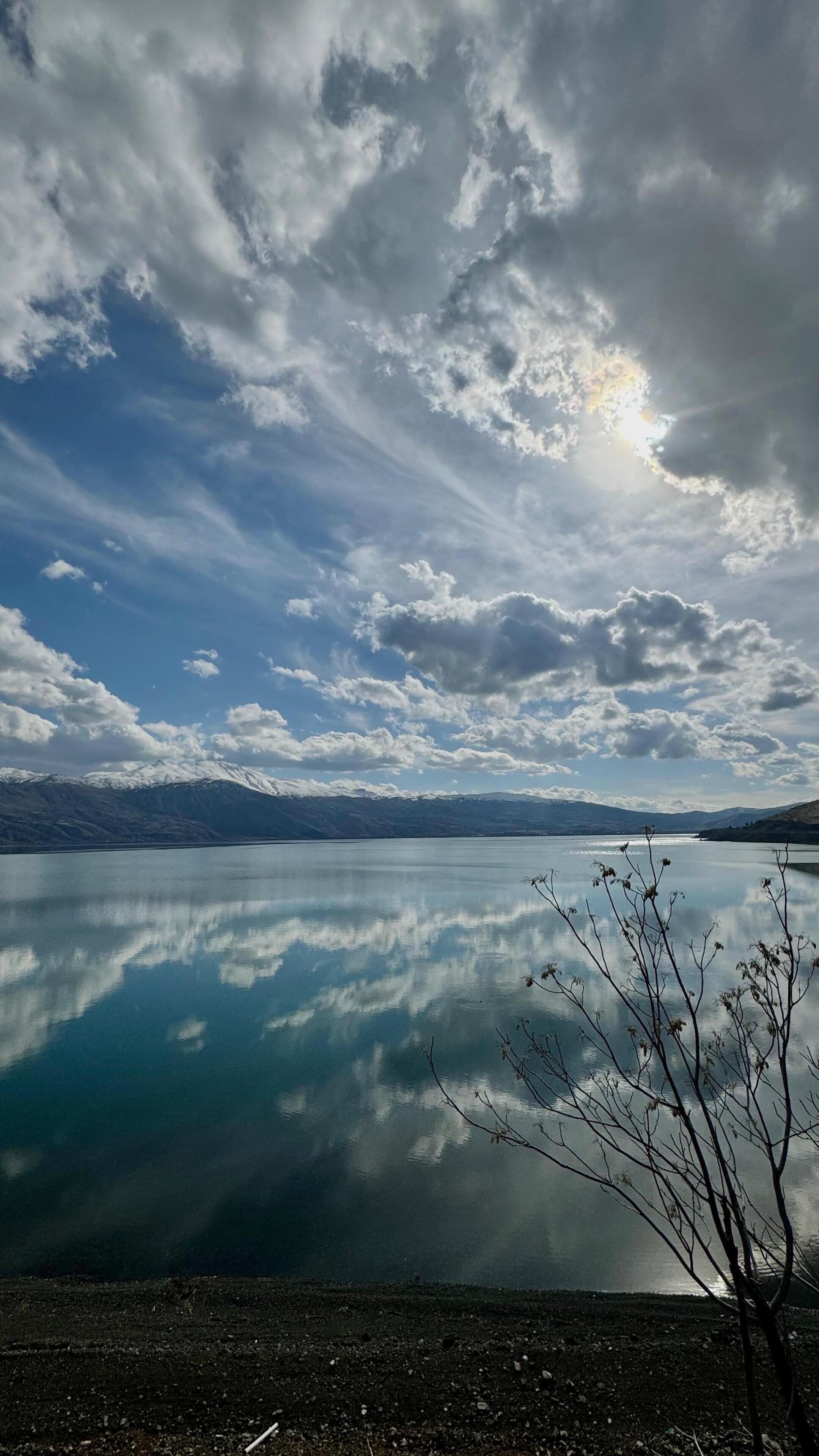 A calm lake with a clear reflection of the sky and mountains in the background.