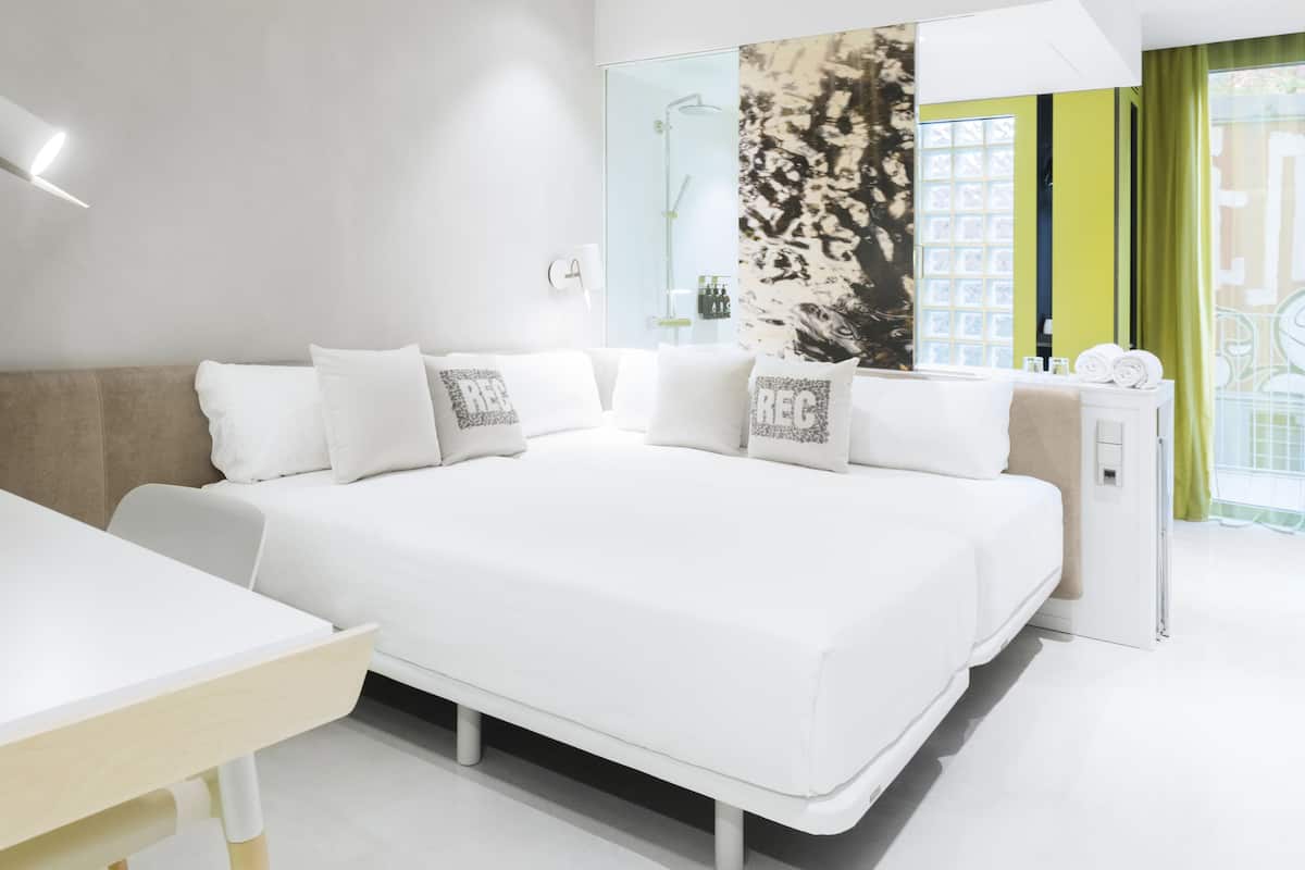 A modern hotel room with a large bed, a bedside table, a mirror, and a window with a view.