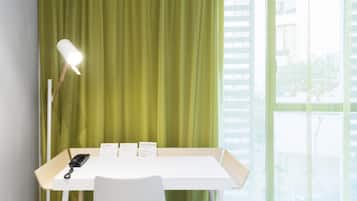 Habitación de hotel con un escritorio, una lámpara y una ventana que ofrece vistas a edificios.