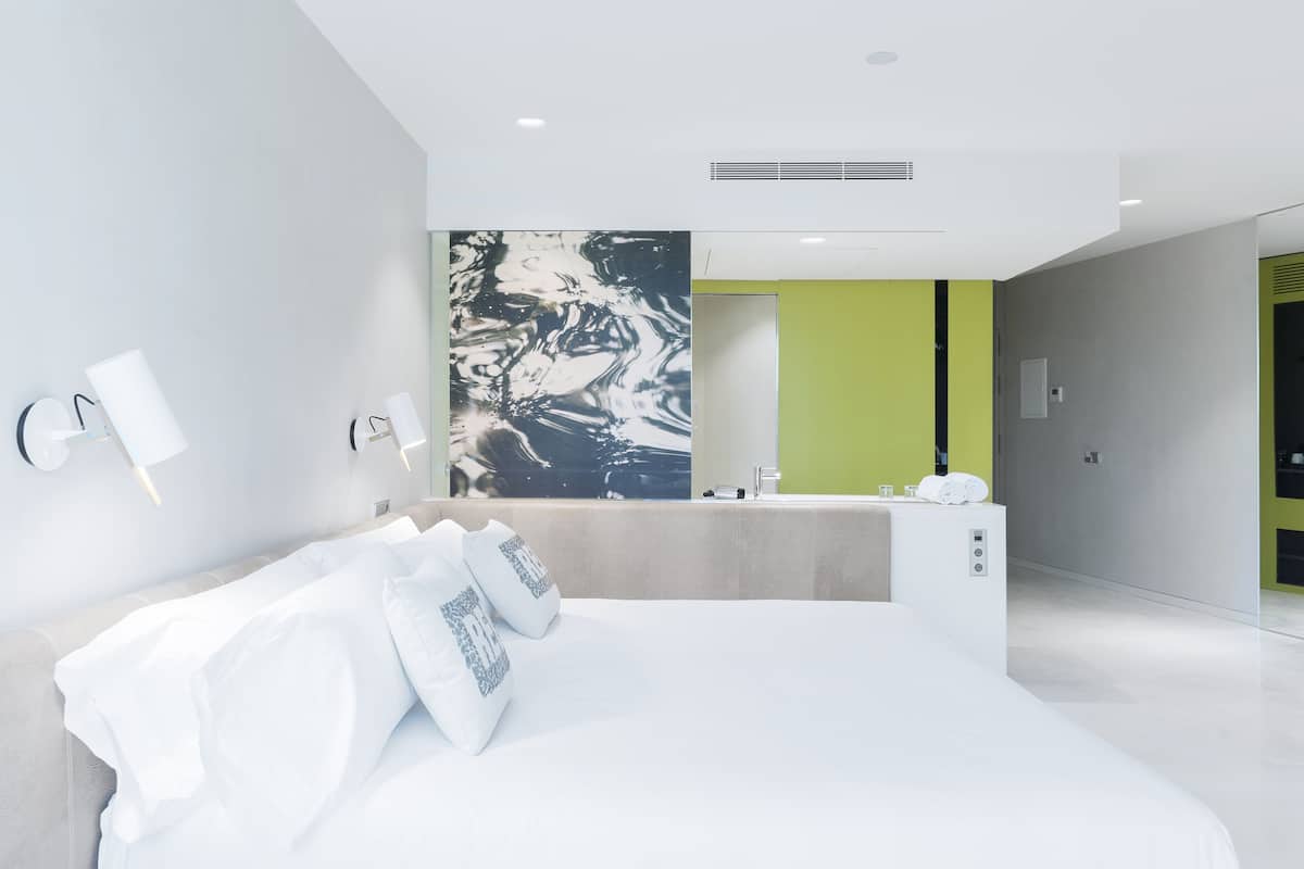 A modern hotel room with a large bed, a bathroom with a green accent wall, and a marble-like artwork above the mirror.
