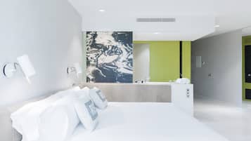Una habitación de hotel moderna con una cama grande, un baño con una pared de acento verde y una obra de arte con apariencia de mármol sobre el espejo.