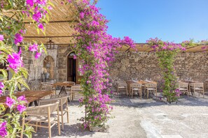An outdoor café with stone walls, wooden tables, and chairs, surrounded by vibrant pink bougainvillea. - BioMasseria Santa Lucia (Alessano)