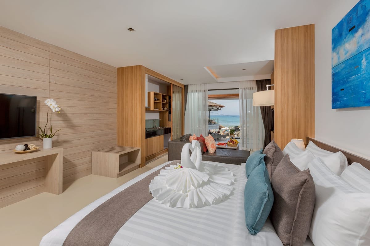 A modern hotel room with a large bed, a TV, a desk, and a view of the sea.
