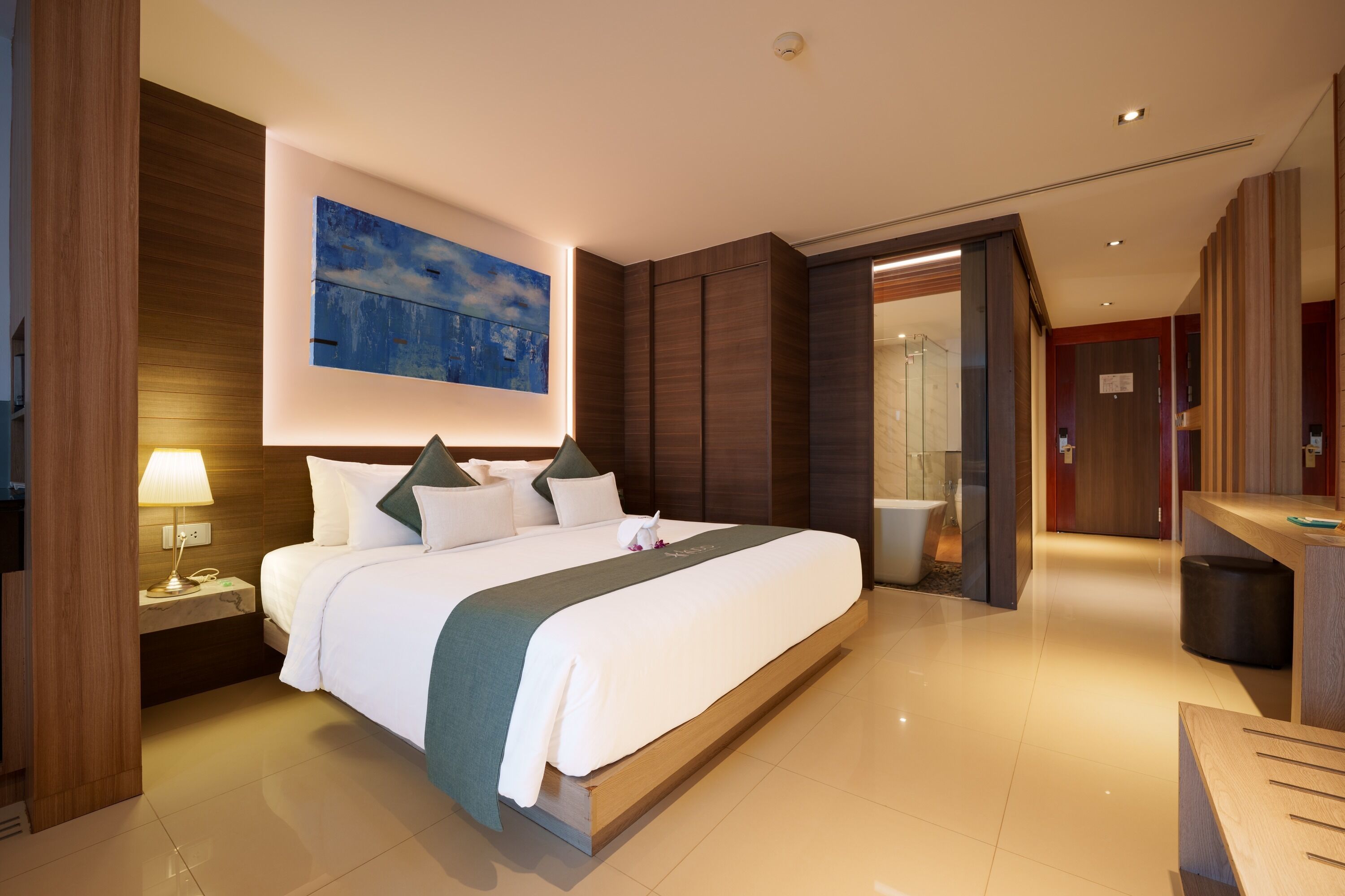 A hotel room with a large bed, a desk, a bathroom, and a view of the outside.
