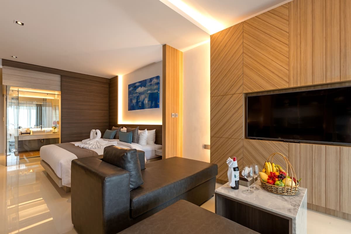 A modern hotel room with a large bed, a sofa, a TV, and a fruit basket on the side table.