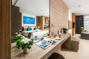 Una habitación de hotel moderna con un mostrador de recepción de madera, una cama con ropa blanca, un cuadro azul en la pared y una cocina al fondo.