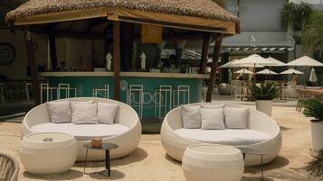 Outdoor wicker furniture with cushions, a thatched umbrella, and a bar area with a sign.
