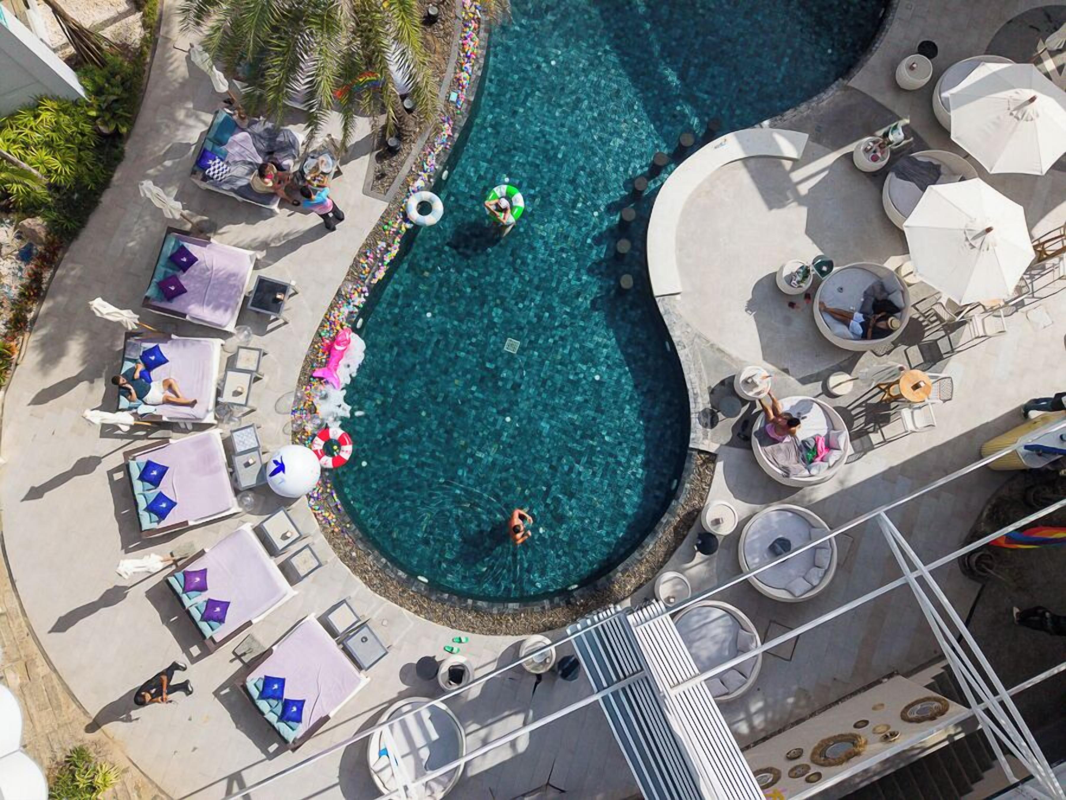 An aerial view of a hotel pool area with sun loungers, umbrellas, and a circular pool.