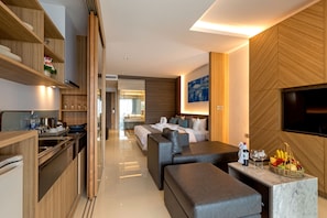 Une chambre d’hôtel moderne dotée d’une cuisine, d’un coin repas, d’un espace de vie avec un canapé et un pouf, d’une télévision à écran plat et d’une grande fenêtre.