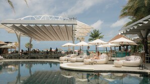 Zona junto a la piscina con sillones de descanso y sombrillas, un bar y vista al océano.