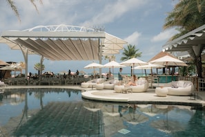 Ein Poolbereich mit Liegestühlen und Sonnenschirmen, eine Bar und Meerblick.