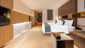 A modern hotel room with a large bed, a desk, a flat-screen TV, and a bathroom with a glass shower enclosure. - Kudo Hotel & Beach Club (Adults Only) (Patong)