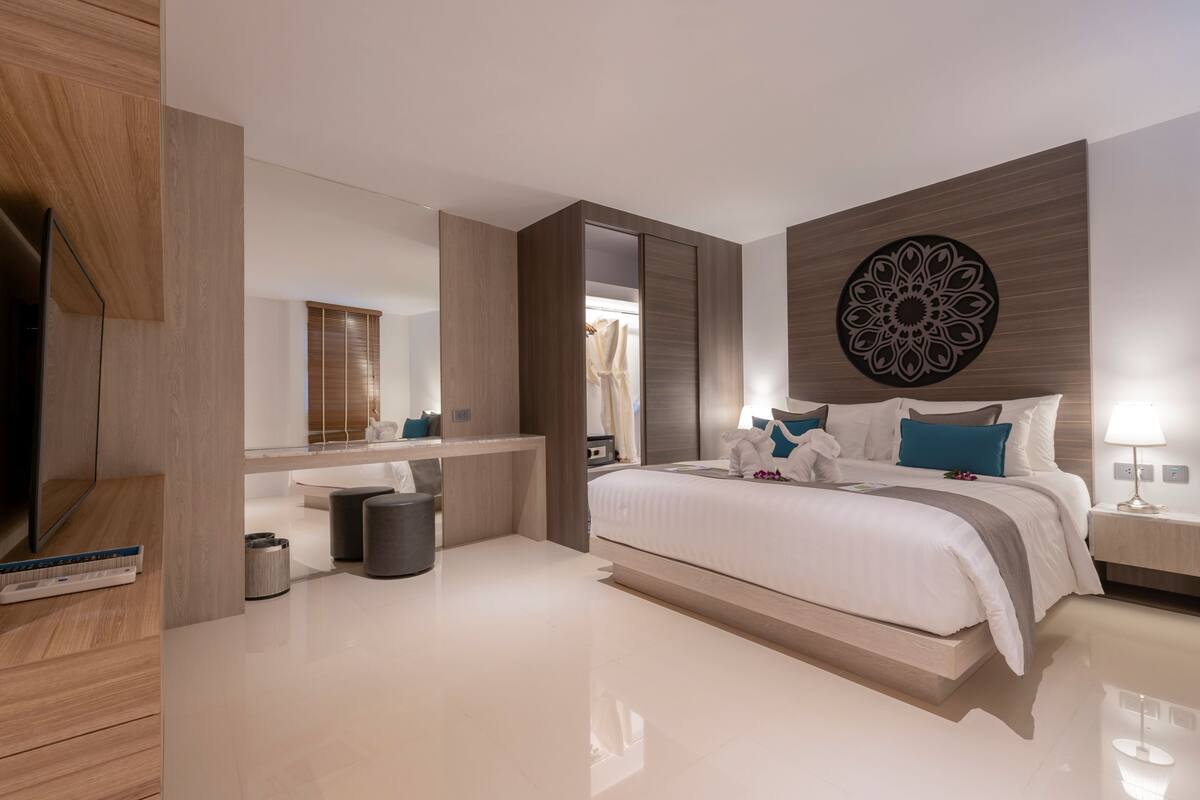 A modern bedroom with a large bed, a vanity, a mirror, and a decorative wall piece.