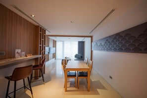 A modern dining area with a wooden table and chairs, a bar area with a counter, and a large wall with a wave pattern. - Kudo Hotel & Beach Club (Adults Only) (Patong)