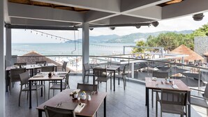 Un área de comedor al aire libre con mesas y sillas, con vista a una playa y al océano.