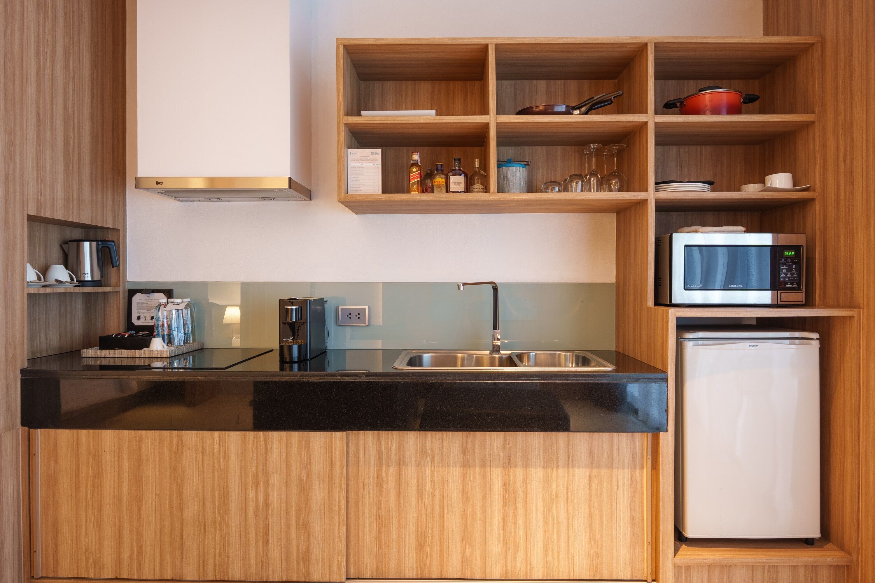 Una cocina compacta con encimera negra, pileta de acero inoxidable y refrigerador blanco.