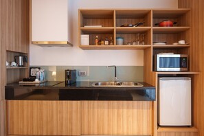 Una cocina compacta con encimera negra, pileta de acero inoxidable y refrigerador blanco.