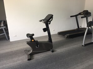 An exercise machine with a handle and a footrest, a treadmill, and a small table with a chair in a room with carpeted flooring. - Kudo Hotel & Beach Club (Adults Only) (Patong)