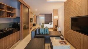 A modern hotel room with a kitchenette, a seating area with cushions, a flat-screen TV, and a large window. - Kudo Hotel & Beach Club (Adults Only) (Patong)