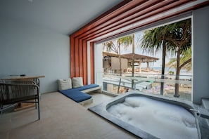 Una habitación moderna con un gran ventanal, una zona de estar con cojines, una mesita y un jacuzzi.