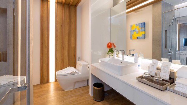 Un baño moderno con techo de madera, un espejo grande y un lavabo blanco con artículos de aseo.