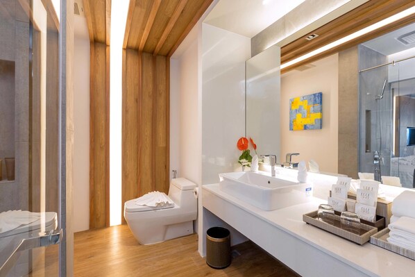 Ein modernes Badezimmer mit Holzboden, einem großen Spiegel und einem weißen Waschbecken mit Pflegeprodukten.