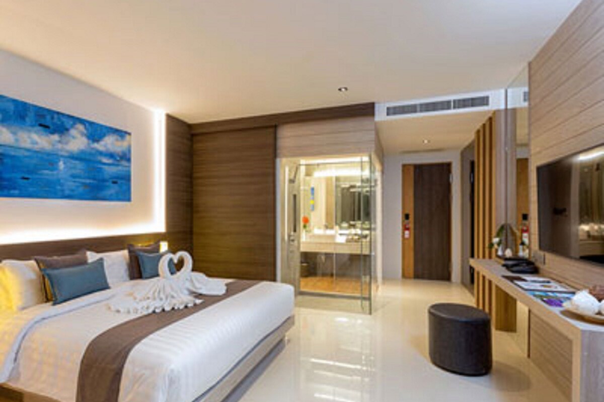 Una habitación de hotel moderna con una cama grande, un baño con ducha de vidrio y un tocador de madera con espejo.