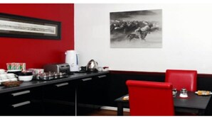 A dining area with a black table, red chairs, and a framed picture on the wall. - The Admirals Inn Guest House (Bracknell)