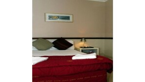 A hotel room with a bed, pillows, a nightstand with a lamp, and a framed picture on the wall. - The Admirals Inn Guest House (Bracknell)