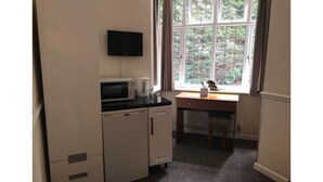 A compact kitchenette with a microwave, coffee maker, and a small table with a tissue box. - The Admirals Inn Guest House (Bracknell)