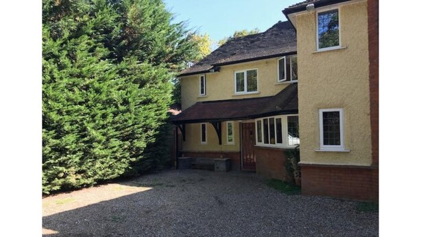 A two-story house with a gravel driveway and a large evergreen tree in the foreground. - The Admirals Inn Guest House (Bracknell)