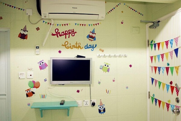 A room with a television, a small table, and a wall decorated with birthday-themed stickers and bunting.