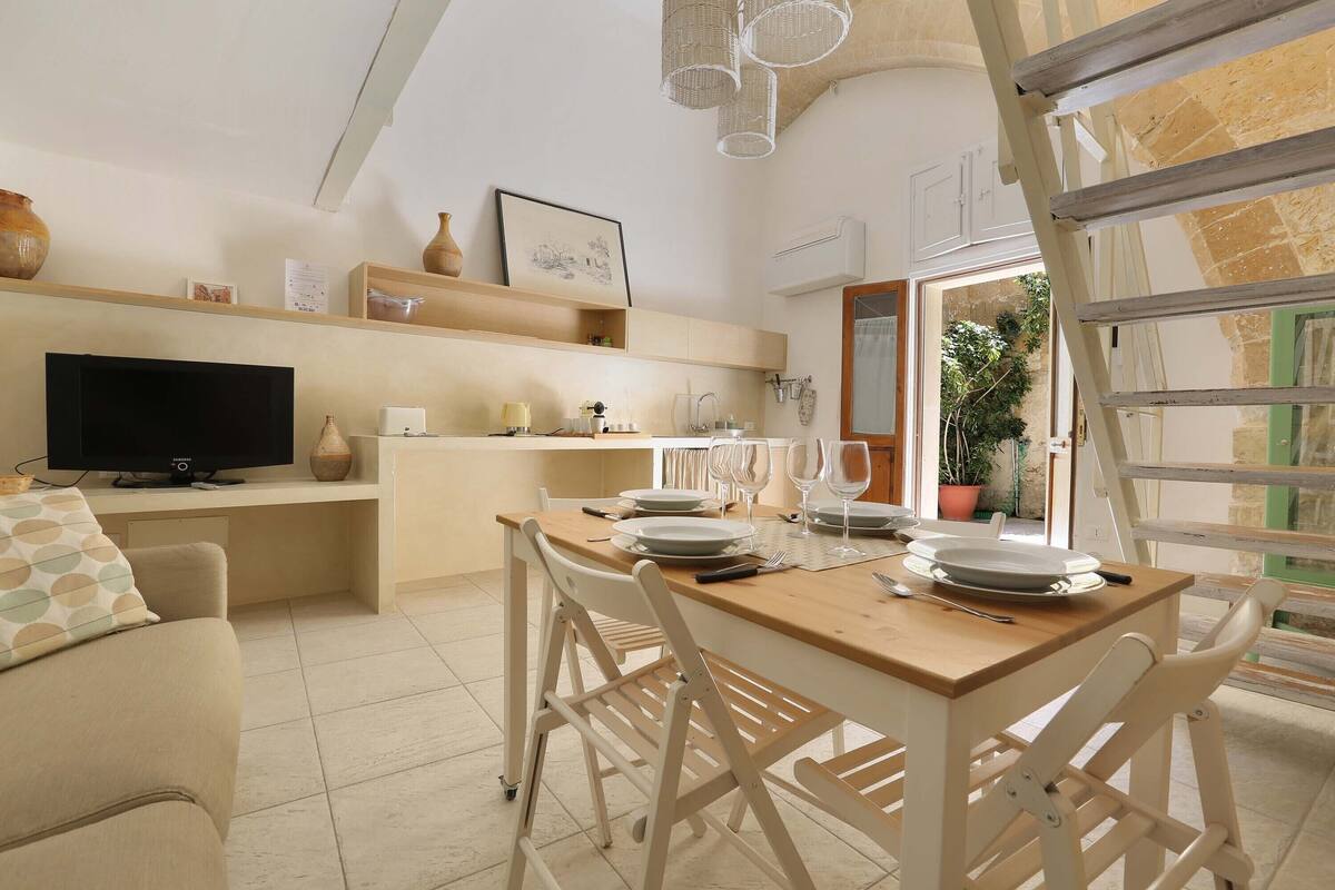 A modern kitchen with a dining area, a TV, and a large window.