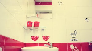 Une salle de bain avec un lavabo blanc, des carreaux rouges et blancs, un miroir et un panneau indiquant les toilettes.