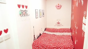 Une chambre à coucher avec un lit recouvert d’une couvre-lit à pois rouges, un porte-manteau mural avec des cintres, une décoration en forme de couronne et un tableau encadré orné d’un motif de couronne.