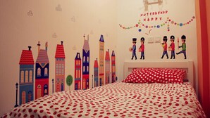 Une chambre à coucher avec un lit, une couvre-lit à pois, un oreiller rouge et un mur décoré de bâtiments colorés et de figurines de casse-noisettes.