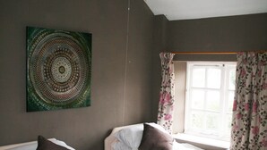 Une chambre avec deux lits simples, une fenêtre ornée de rideaux à motifs floraux et une œuvre d’art accrochée au mur.