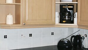 Une cuisine avec des meubles de rangement en bois, une machine à café et une bouilloire posées sur le plan de travail.