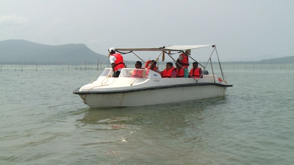 Um barco com passageiros usando coletes salva-vidas em águas calmas.